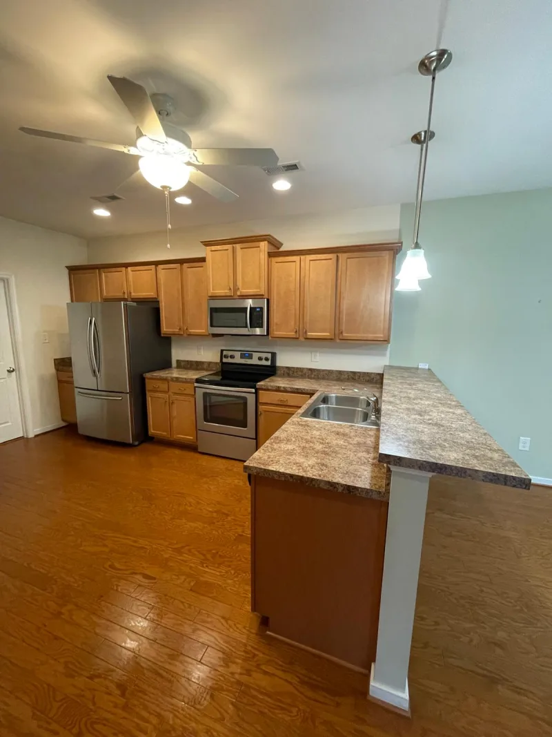 Clean open kitchen with wood cabinets, stainless steel appliances, and polished floors