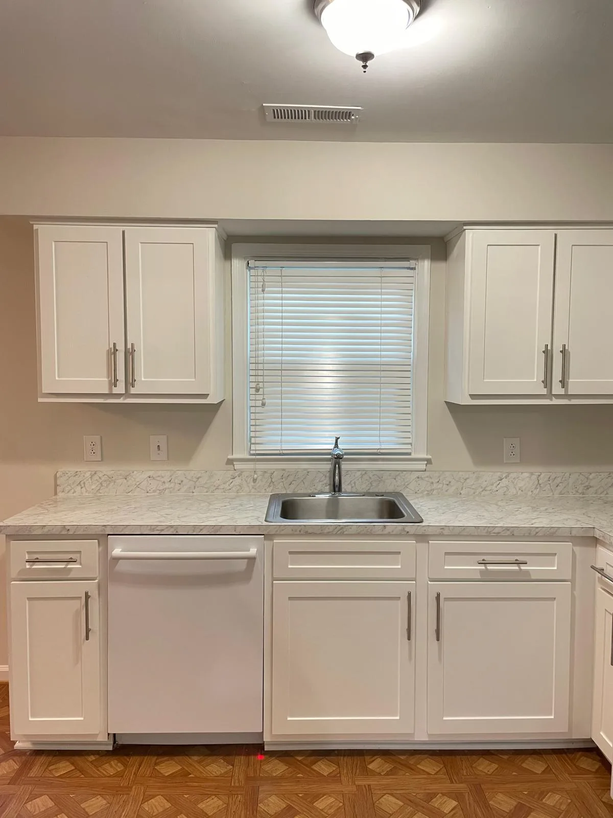 Clean white kitchen with a stainless steel sink under a window